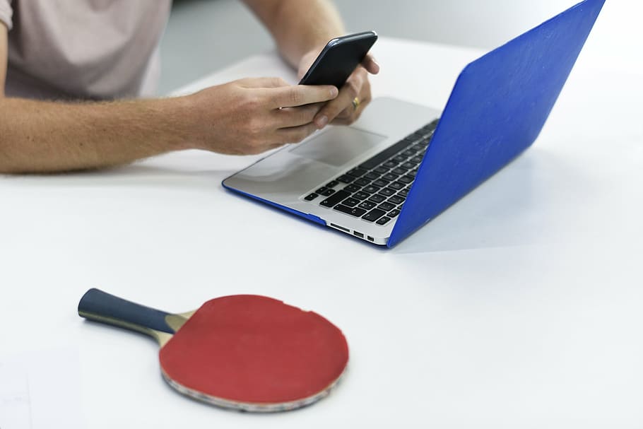person holding smartphone beside MacBook and table tennis paddle HD wallpaper