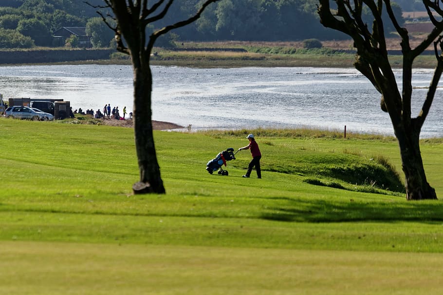 man pushing trolley golf bag in an open field at daytime, golf course HD wallpaper