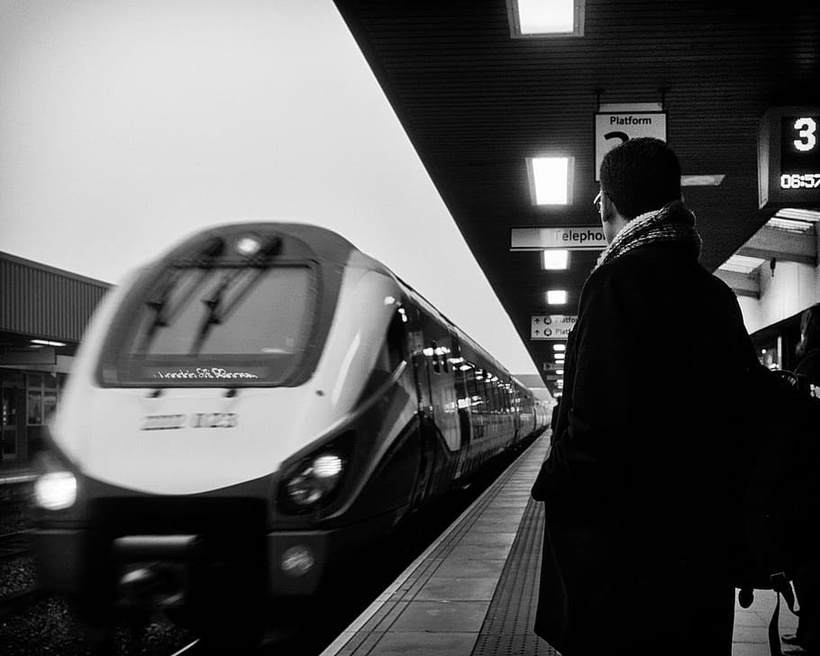 man standing beside moving train, grayscale photo of person standing near train