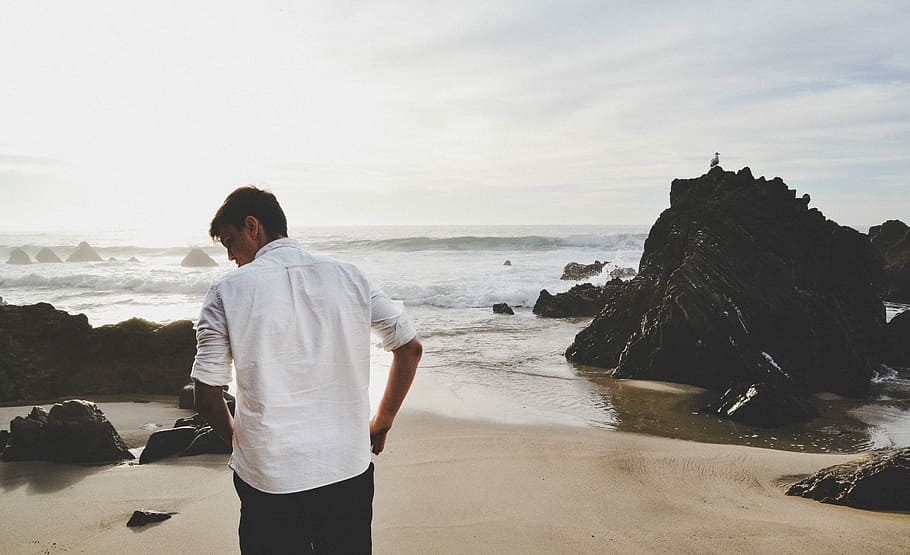 man standing on seashore, man in white dress shirt standing in front of beach during daytime HD wallpaper