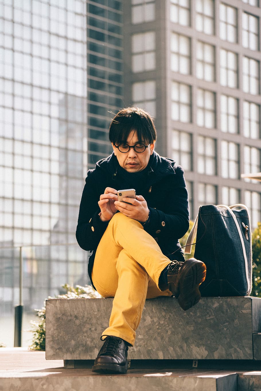 man using smartphone sitting on concrete bench, man sitting on bench while using phone HD wallpaper