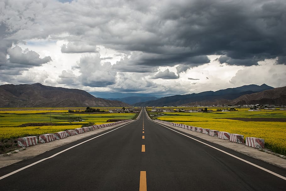 gray concrete road between grass fields under cumulus clouds HD wallpaper