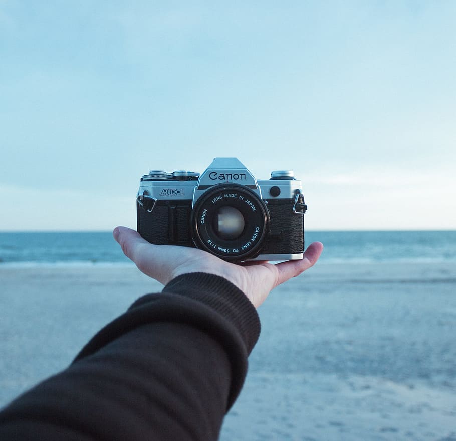 person holding black and gray Canon AE-1 bridge camera, person holding Canon MILC HD wallpaper