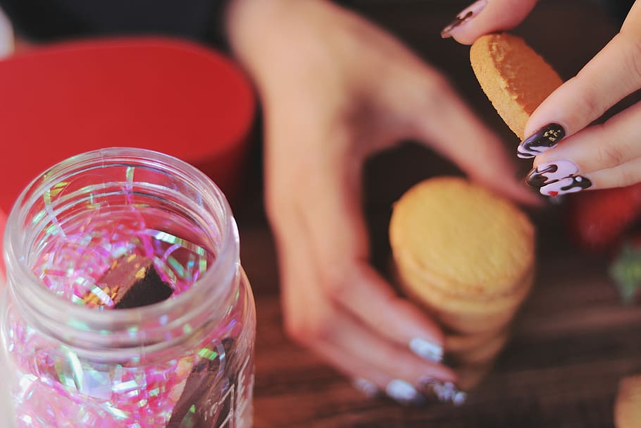 person holding baked cookies near clear glass cookie container HD wallpaper