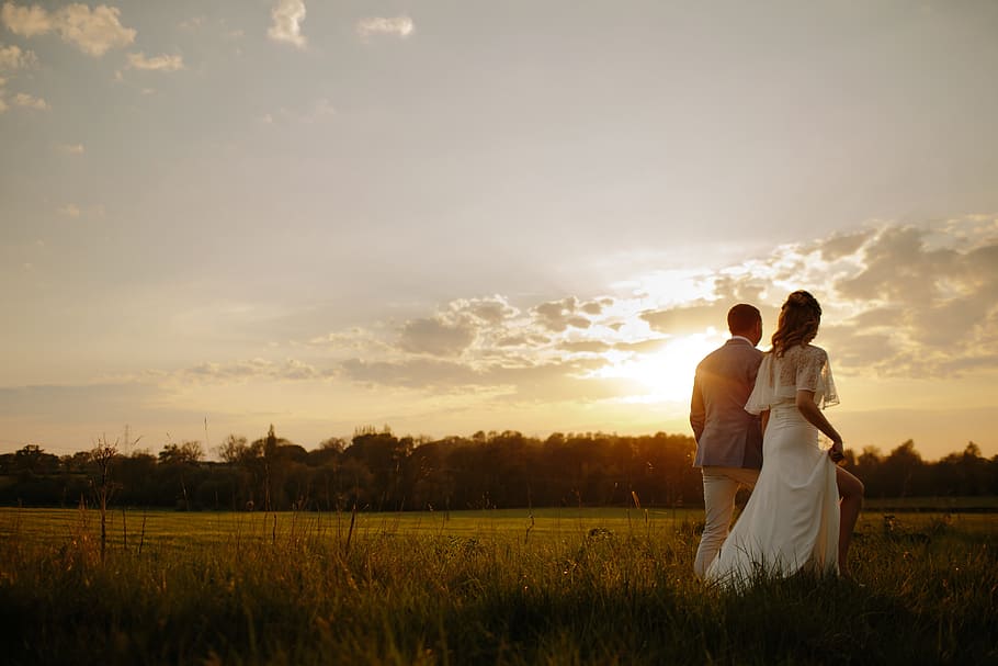 Couple, bride and groom walks on grass with sunrise background