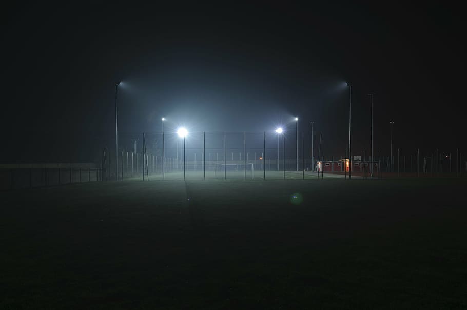 lights turned on in green field surrounded with fence at nighttime HD wallpaper