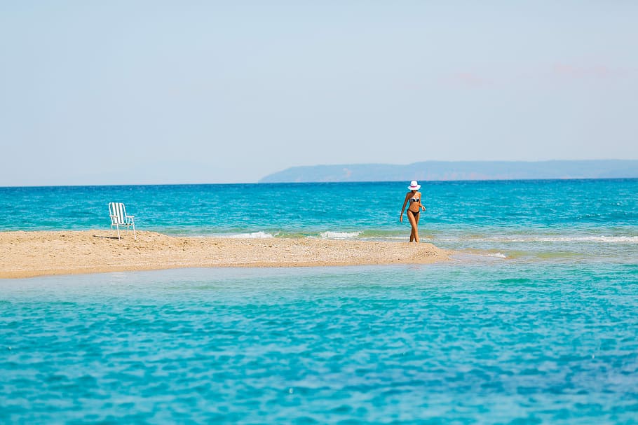 woman standing on sand bar during daytime, woman standing on brown sand surrounded by body of water under blue sky during daytime HD wallpaper