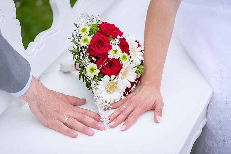 red rose, white daisies, and green mums flower bouquet beside man and woman hands