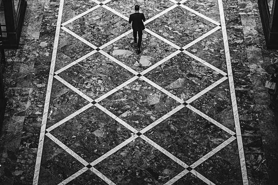 A male walking down a diamond-patterned street., grayscale photography of person walking on soil, HD wallpaper