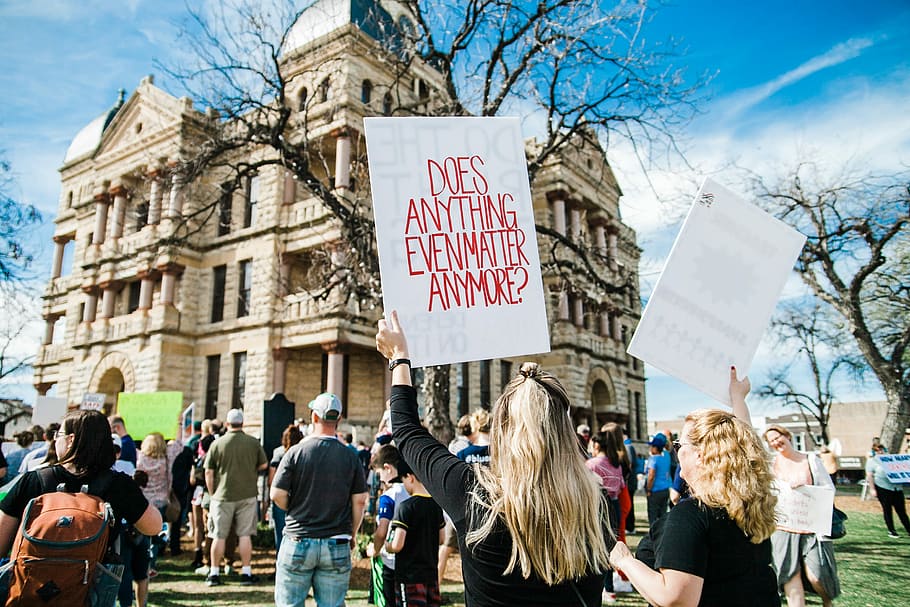 woman holding does anything even matter anymore? signage near building at daytime, woman raising placard with does anything even matter anymore? print HD wallpaper