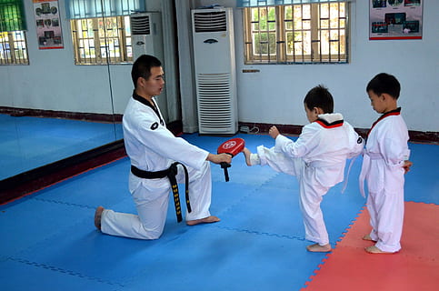 man wearing karate gi teaching child to kick inside training room HD wallpaper