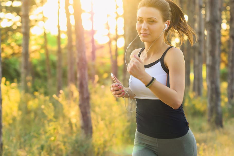 Girl jogging/running exercises workout in the forest using earphones connected to her mobile iPhone smartphone, HD wallpaper
