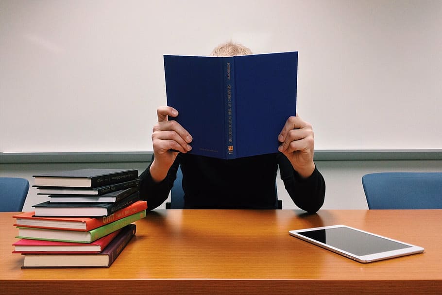 person holding blue book leaning on brown wooden desk, read HD wallpaper