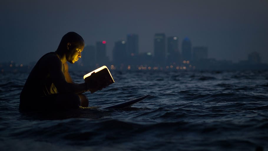 man reading book while sitting on surfboard, person, lamp, body