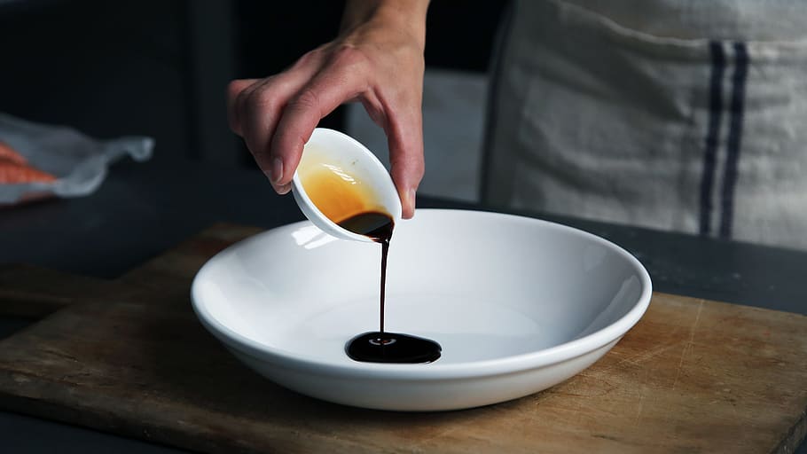 person dripping black liquid from small white ceramic bowl to big white ceramic bowl, person pouring soy sauce on plate HD wallpaper