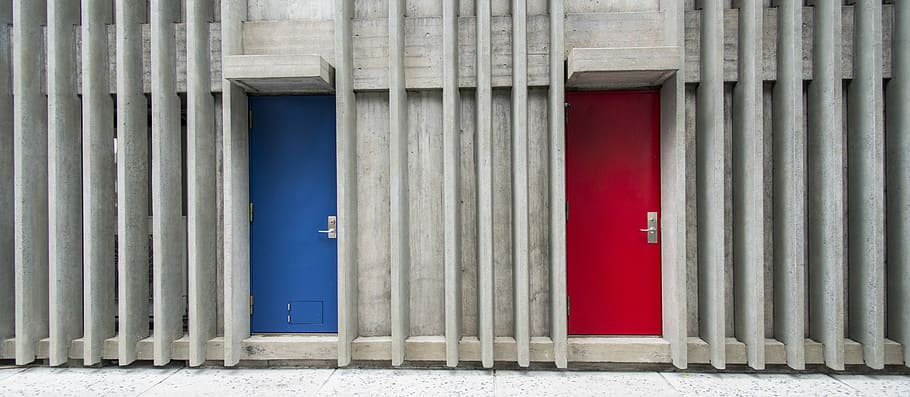 two blue and red door closed during daytime, two red and blue doors between slatted grey wooden frames
