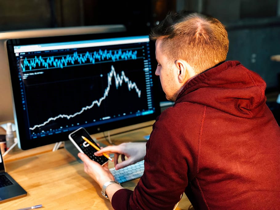man holding black smartphone with flat screen monitor in front, man holding smartphone sitting infront of computer monitor HD wallpaper