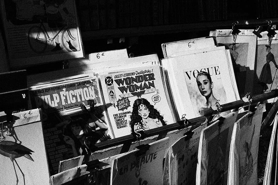 grayscale photo of magazines on rack, Wonder Woman and Vogue magazines