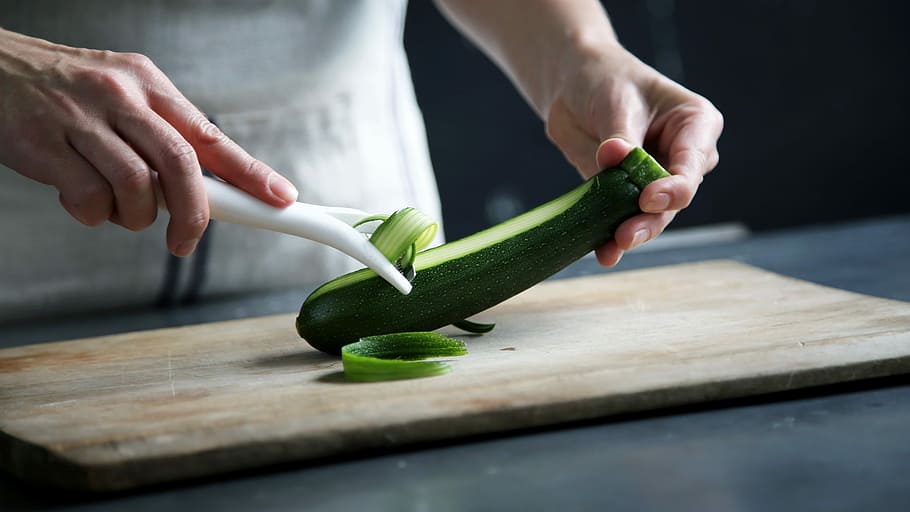person pealing green cucumber inside room, man peeling cucumber