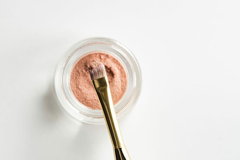 brown makeup brush in front pink powder on glass case, makeup brush with pink powder