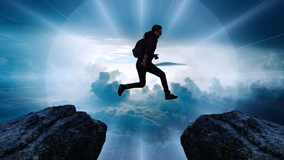 man jumping beside two rocks with background of clouds, cliff