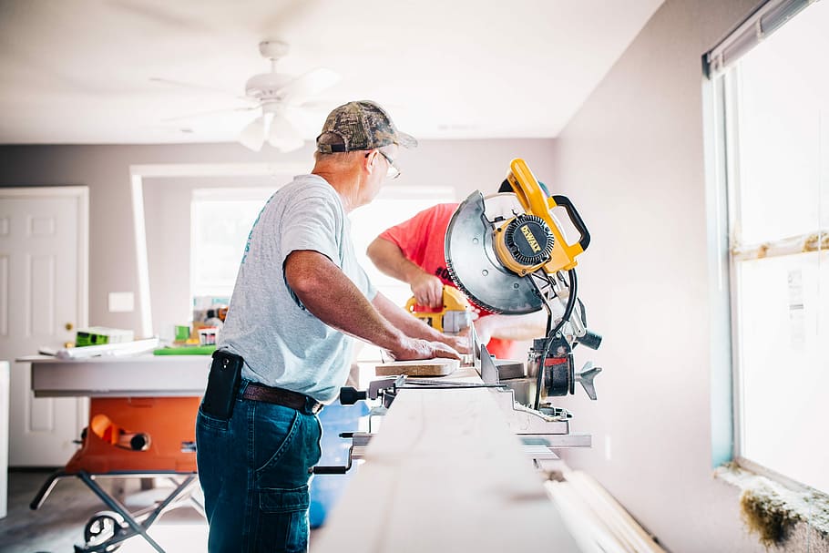 man standing infront of miter saw, man using saw inside room