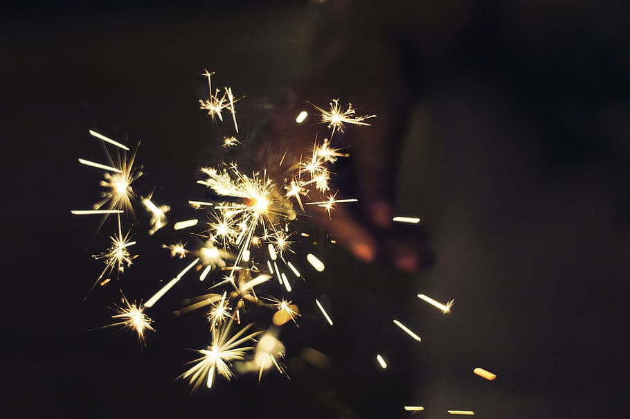 person holding sparkler, brown spark firecracker, firework, hand