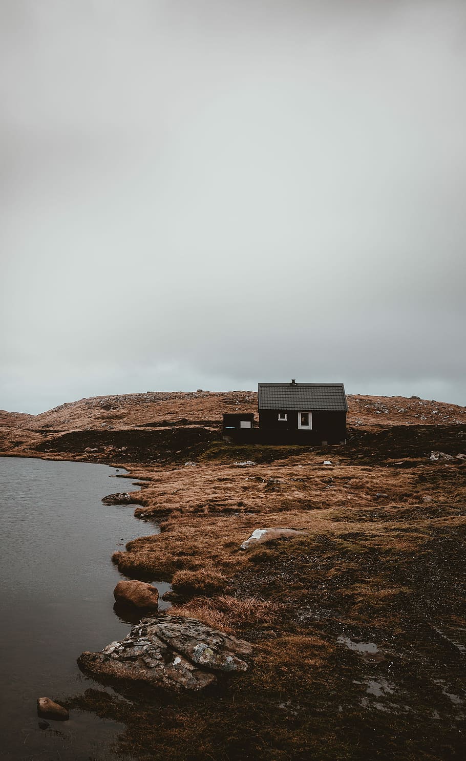 black house in the middle on island, black house on brown grass field near body of water, HD wallpaper