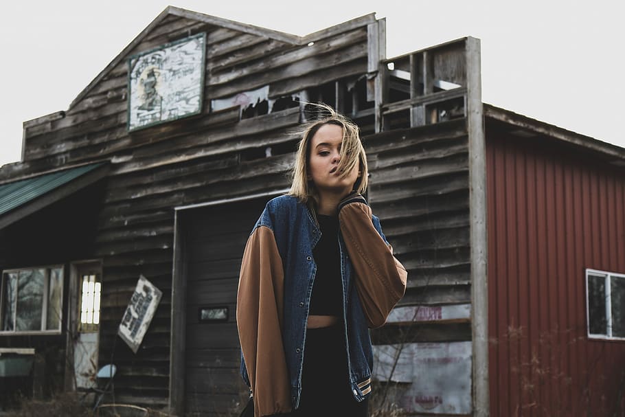 woman holding her neck in front of barn, woman wearing blue and brown jacket standing near house HD wallpaper