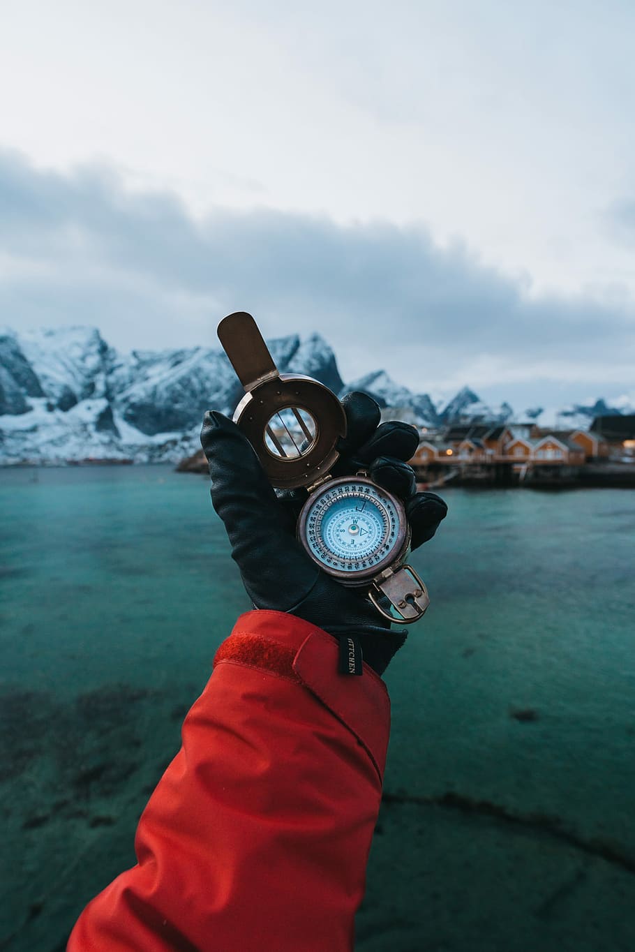 round gray compass, person holding up brass-colored compass at eye level outside with mountain range in background during twilight HD wallpaper