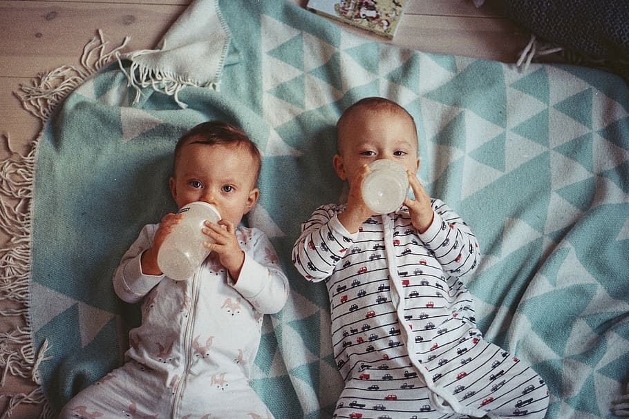 two babies lying on teal textile, two toddler laying on teal textile while drinking feeding bottles, HD wallpaper