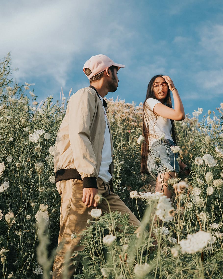 man and woman climbing white wild carrot flower fields, couple walking through white petaled flowers during daytime