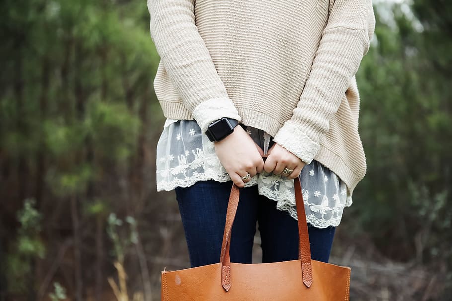 woman standing holding a brown leather tote bag, person holding brown leather bag