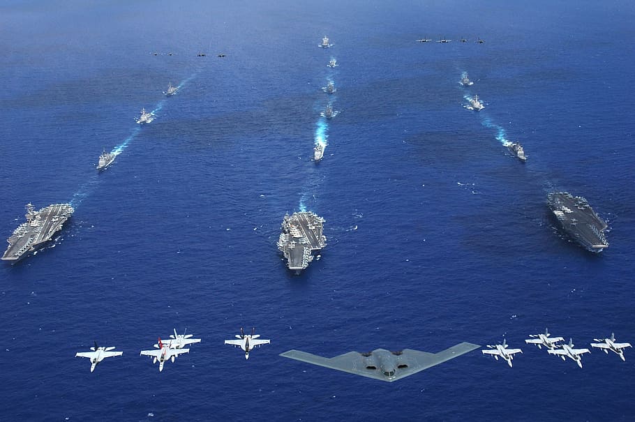 stealth fighter and jet plane over aircraft carrier on large blue body of water at daytime