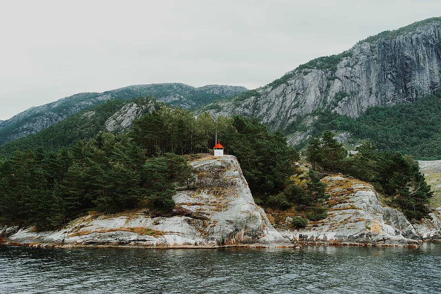 white rock formation, white and red house near tall trees and calm body of water at daytime HD wallpaper