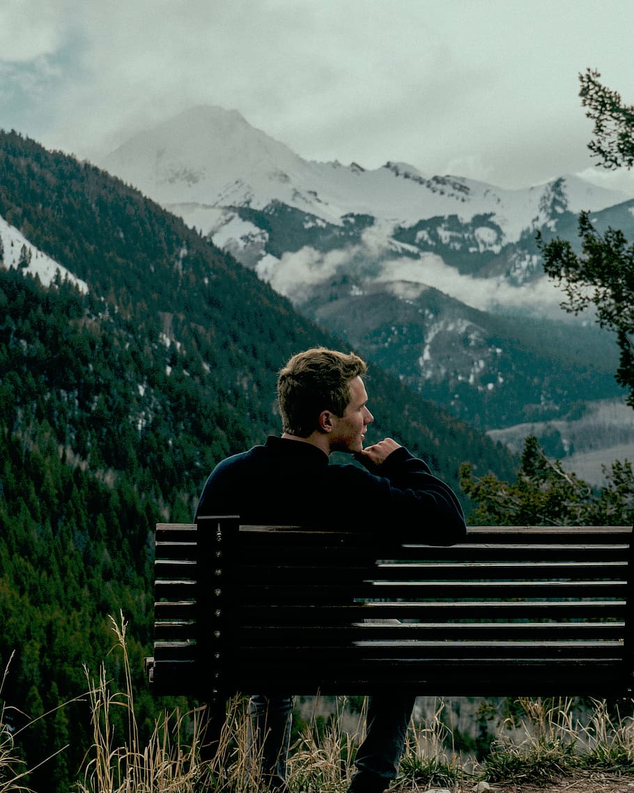 man sitting on bench in front of mountain during daytime, mountains HD wallpaper