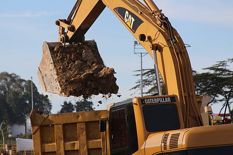 yellow Caterpillar excavator bucket filled with soil above yellow dump truck at daytime HD wallpaper