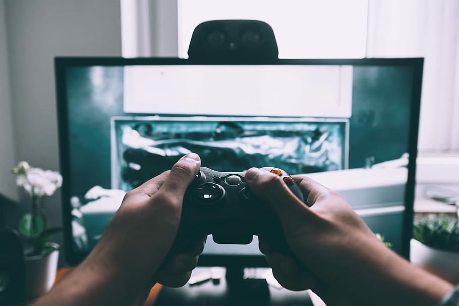 person holding game controller in-front of television, person holding game controller while playing in front turned on flat screen TV inside entertainment room