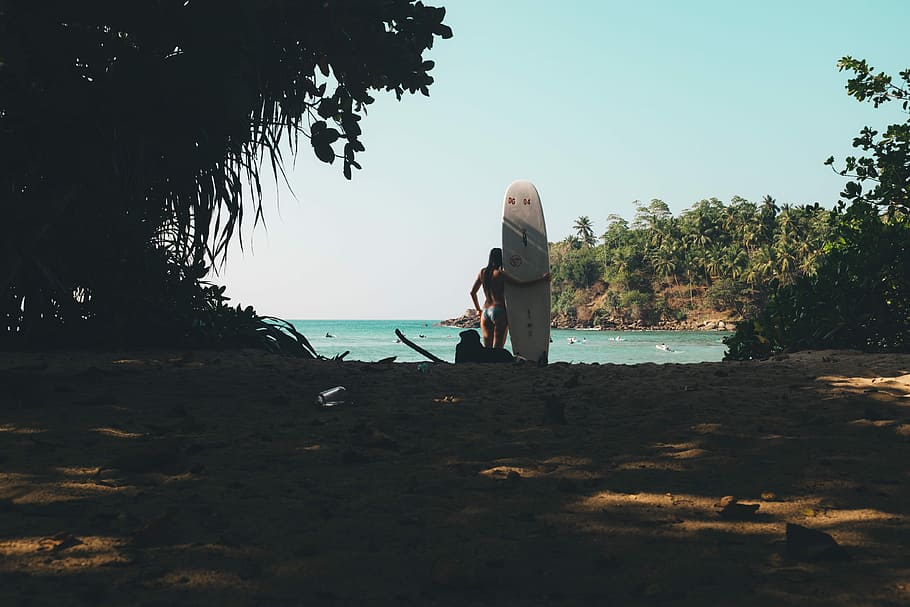 person holding white surfboard standing on seashore during daytime, landscape photography of woman holding surfboard near sea HD wallpaper