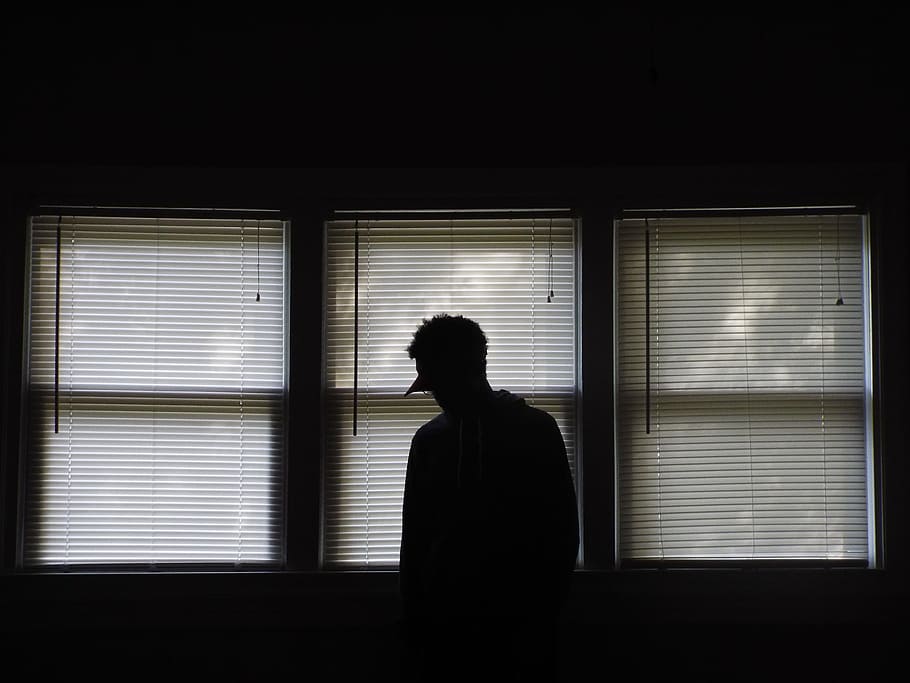 man standing infront of window blinds, silhouette of person standing beside white window blinds inside room