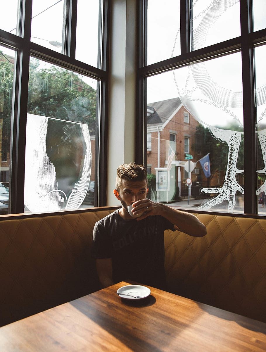 man in grey T-shirt sipping on white ceramic cup sitting on yellow leather sofa near window during daytime HD wallpaper