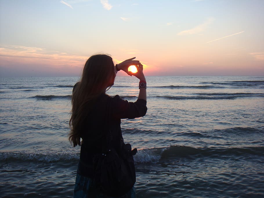 woman with black shirt hand forming hearts by the seashore, beach