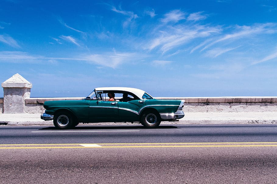green coupe on gray asphalt road, person driving classic car on concrete road