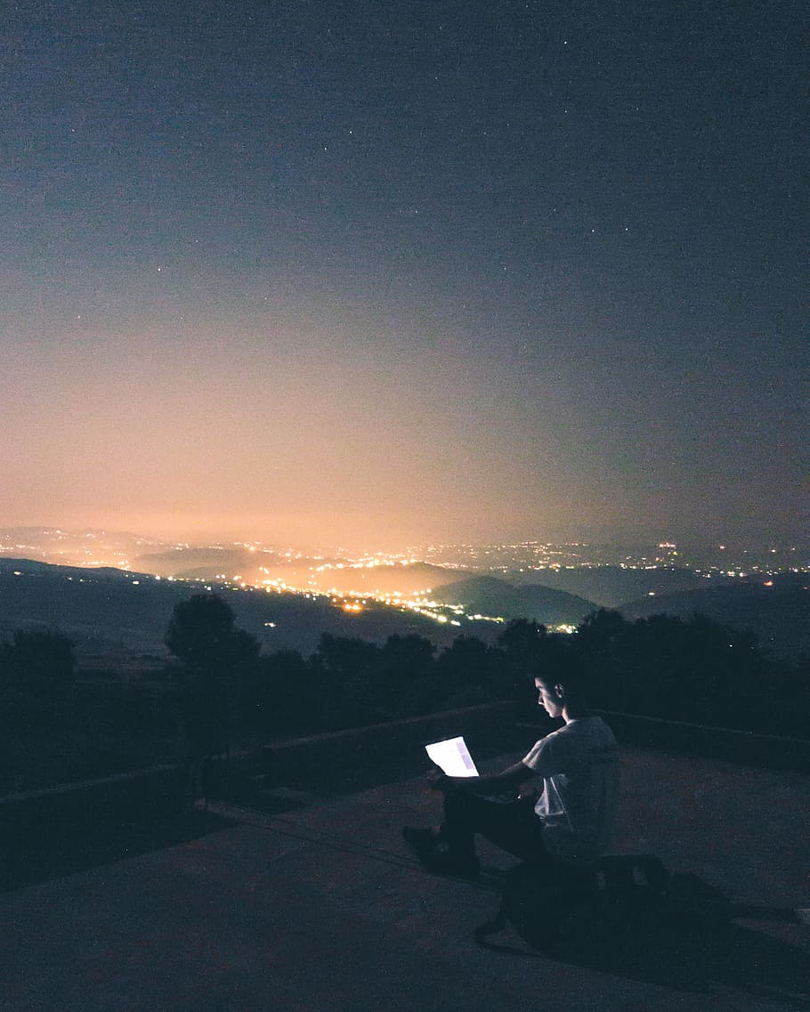 portrait photography of man sitting in front of mountains while using laptop