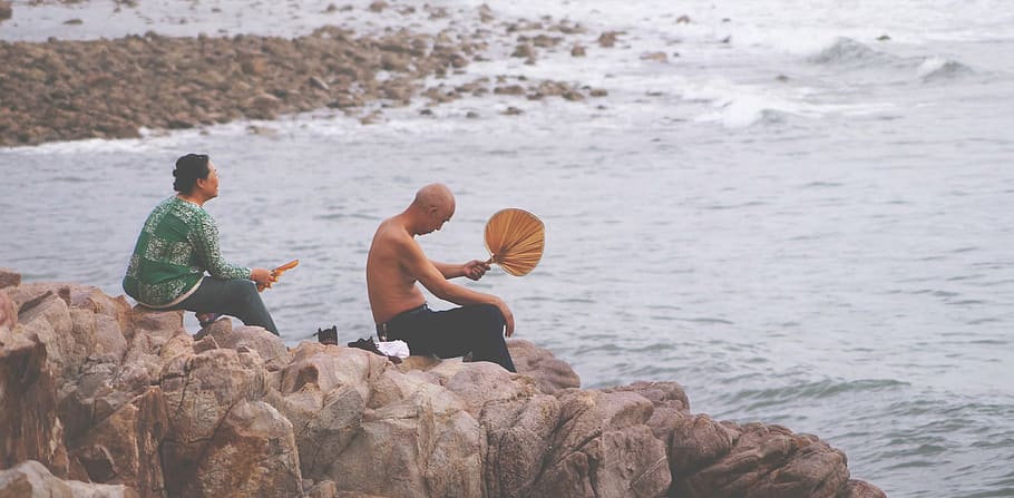 two person sitting on rock facing sea, two men sitting on rock beside body of water, HD wallpaper
