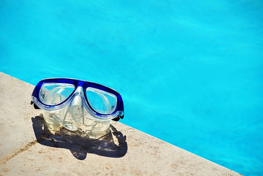 blue framed swimming goggles near pool at daytime, clear swimming goggle on gray concrete pavement near body of water HD wallpaper