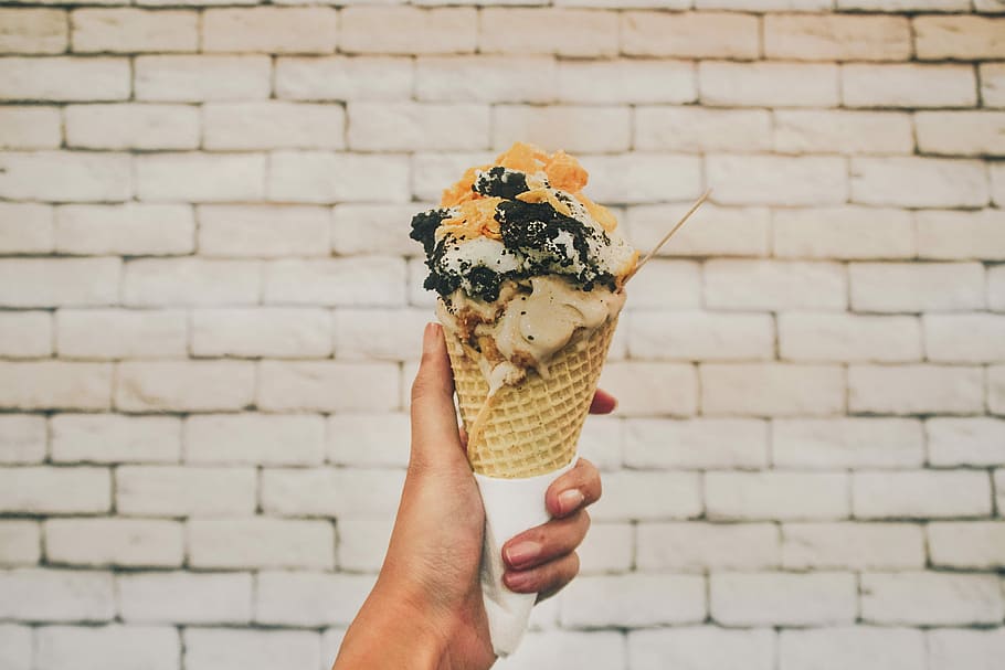 person holding ice cream, cone, brick, wall, eat, hand, gelato