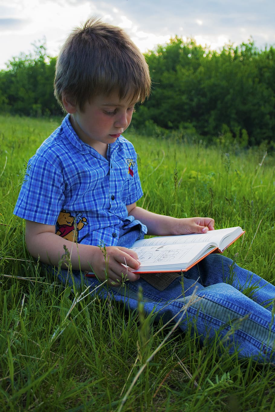 boy sitting on green grass field while reading book during daytime, HD wallpaper