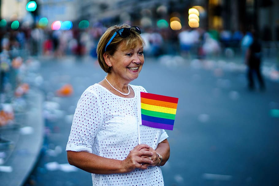 woman smiling holding LGBT flaglet, woman holding rainbow flaglet on road during daytime, HD wallpaper