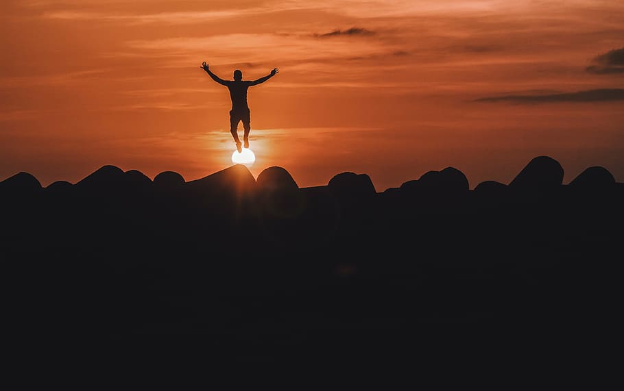 silhouette photo of a person jumping on rocks during golden hour HD wallpaper